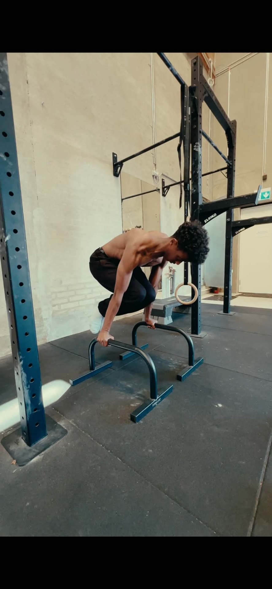 Athletic man performing a dip exercise on parallel bars inside a gym, leaning forward with focused posture.